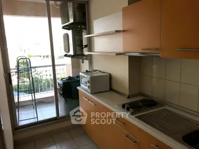 Compact kitchen with orange cabinets and balcony view, featuring a microwave and electric stove.