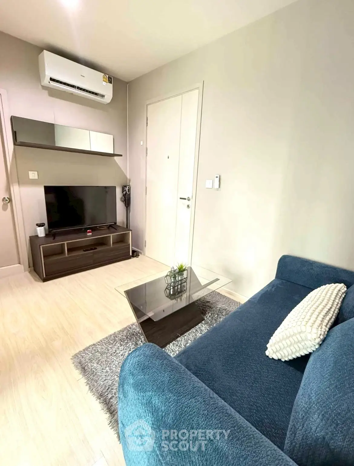 Cozy living room with modern decor, featuring a plush blue sofa, sleek TV unit, and stylish glass coffee table.