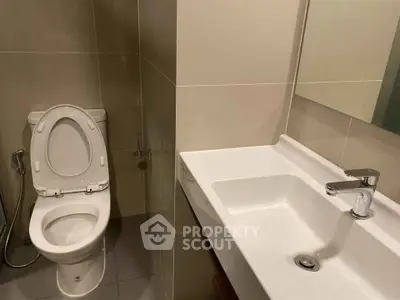 Modern bathroom with sleek fixtures and neutral tiles, featuring a toilet and a stylish sink.