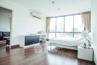 Spacious bedroom with large window and city view, featuring modern decor and wooden flooring.