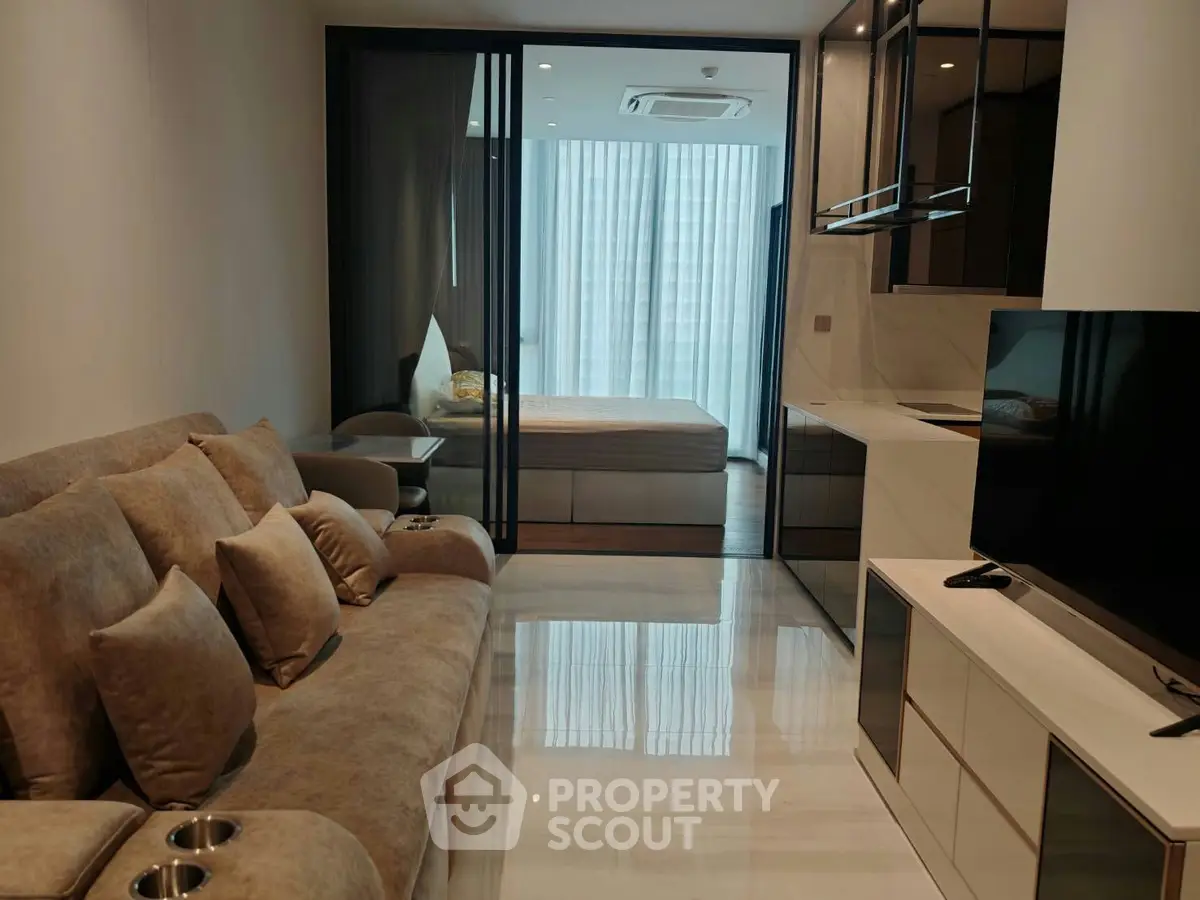 Modern studio apartment with sleek design, featuring cozy living area and stylish bedroom separated by glass doors.