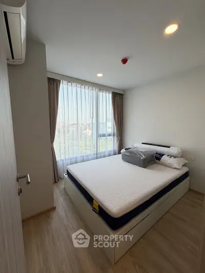 Modern bedroom with large window and natural light, featuring a comfortable bed and wooden flooring.