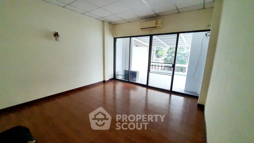 Spacious living room with wooden flooring and large glass doors leading to a balcony.