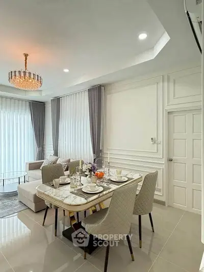 Elegant living room with dining area, featuring modern decor and luxurious chandelier.