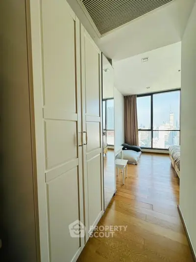 Modern bedroom with city view, wooden flooring, and sleek wardrobe design.