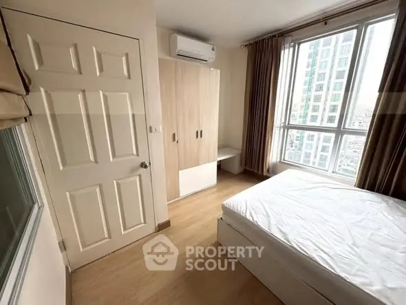 Bright and cozy bedroom with large window and modern furnishings in a high-rise apartment.