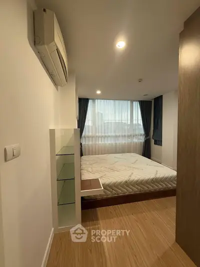 Modern bedroom with large window and wooden flooring in a stylish apartment.