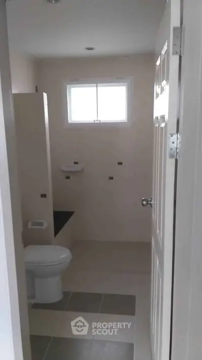 Modern bathroom with neutral tiles and natural light from window.