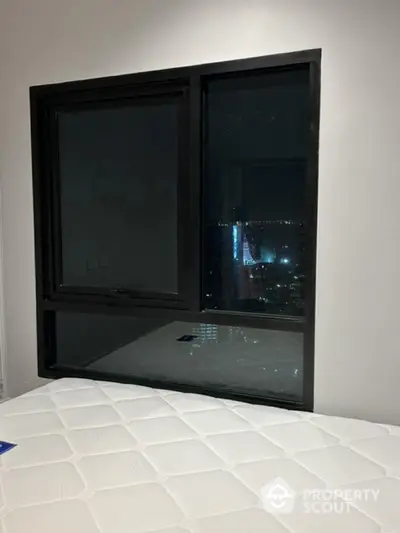 Modern bedroom with large window offering stunning city view at night.