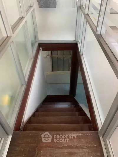 Modern staircase with wooden steps and glass panel walls in a contemporary home.