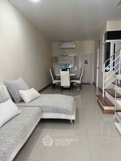 Spacious living room with modern furniture and dining area, featuring sleek tiled flooring and elegant staircase.