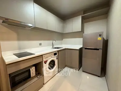 Modern kitchen with sleek cabinetry, washing machine, and stainless steel fridge in a compact layout.