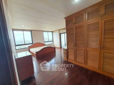 Spacious bedroom with wooden flooring and large windows offering city views.