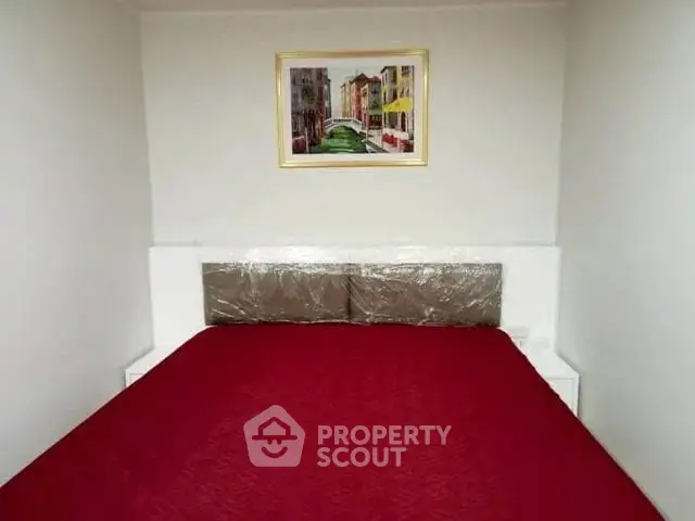 Cozy bedroom with vibrant red bedding and framed artwork, perfect for a comfortable living space.