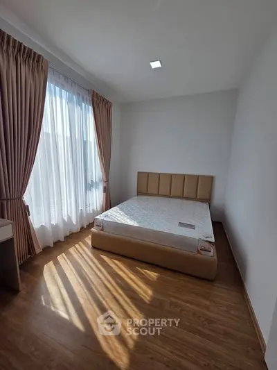 Bright and airy bedroom with large window and elegant curtains, featuring a comfortable bed and wooden flooring.