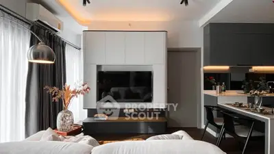 Modern living room with sleek design, featuring a wall-mounted TV, stylish decor, and open kitchen layout.