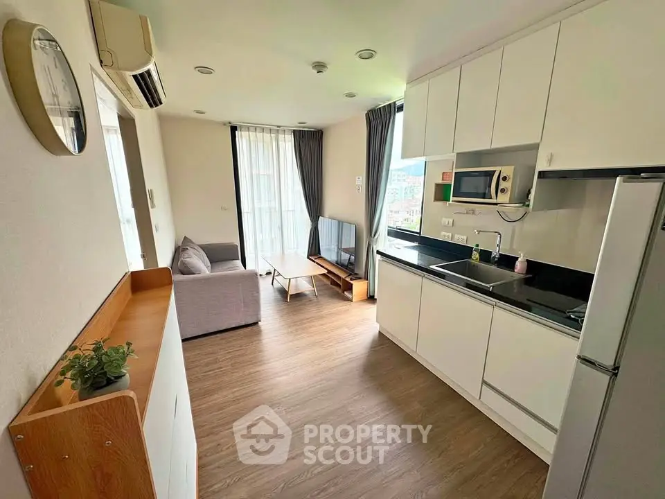 Modern open-layout living room with kitchen, featuring sleek white cabinetry and cozy seating area.