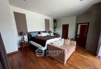 Spacious bedroom with elegant decor and wooden flooring, featuring a cozy seating area and ample natural light.