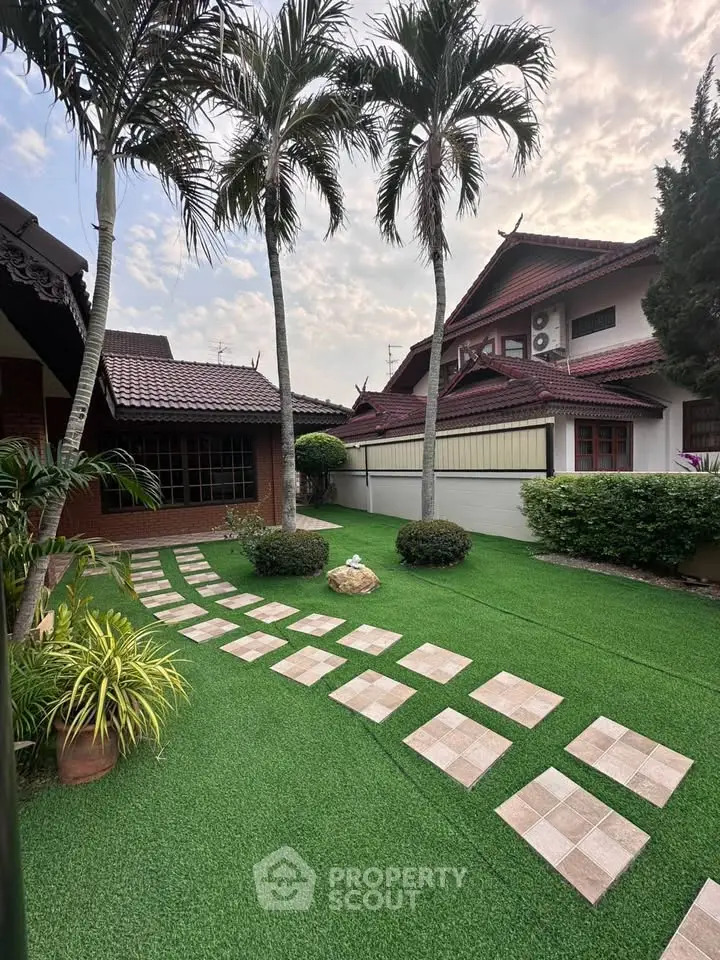 Charming suburban home with lush garden and palm trees, featuring a well-maintained pathway and traditional architecture.