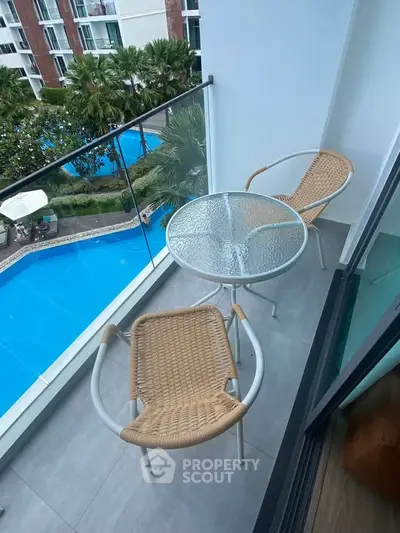 Charming balcony with pool view, featuring cozy seating and glass railing in modern apartment.