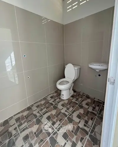 Modern bathroom with tiled walls and floor, featuring a toilet and sink.