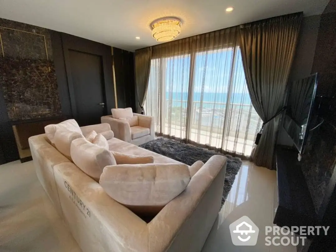 Luxurious beachfront living room with plush sofas, glossy marble floors, and panoramic ocean views through floor-to-ceiling windows, accented by elegant drapery and modern lighting.