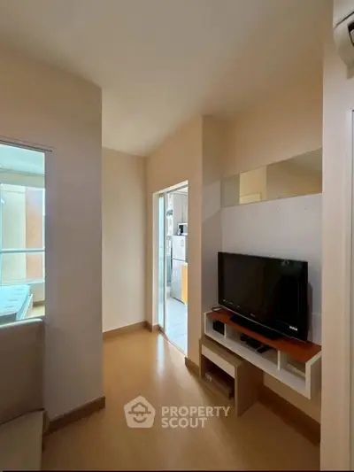Modern living room with TV and wooden flooring, adjacent to a bright kitchen area.