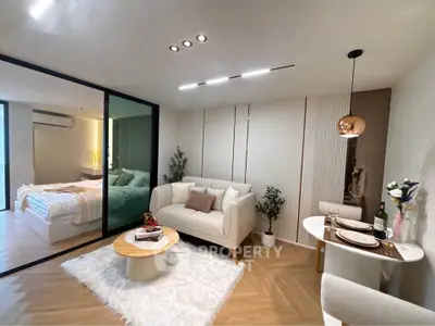 Modern living room with cozy seating and stylish decor adjacent to a bedroom with glass partition.