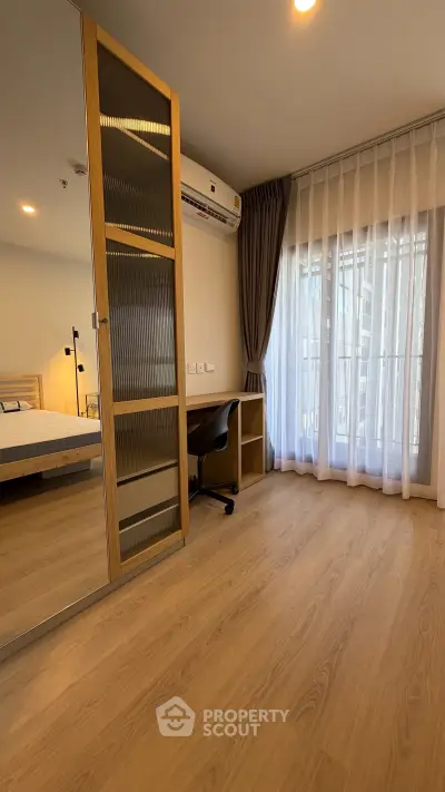 Modern bedroom with wooden flooring, large window, and study desk in a stylish apartment.