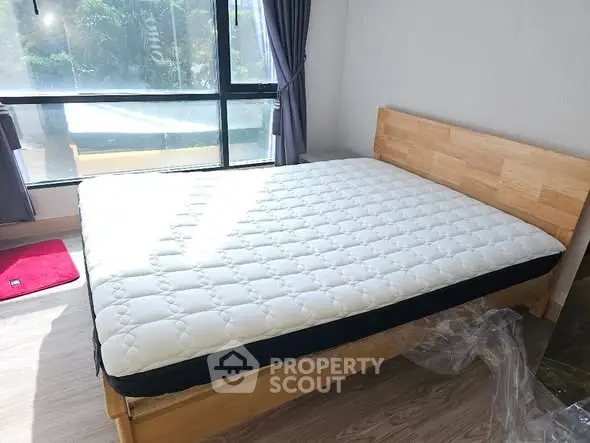 Bright bedroom with large window and wooden bed frame, perfect for relaxation.