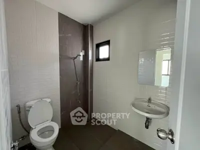 Modern bathroom with sleek design featuring a toilet, sink, and shower area with neutral tiles.
