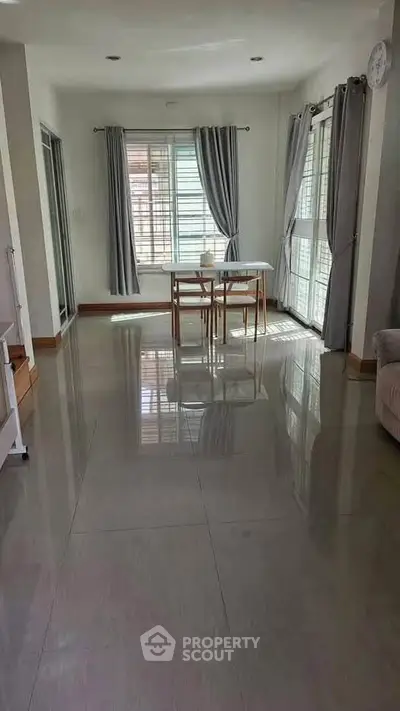 Spacious living room with glossy floors and natural light, featuring modern dining set and large windows.