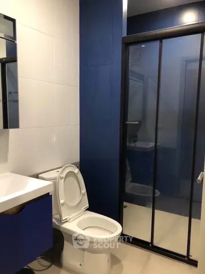 Modern bathroom with sleek blue and white design featuring glass shower enclosure.