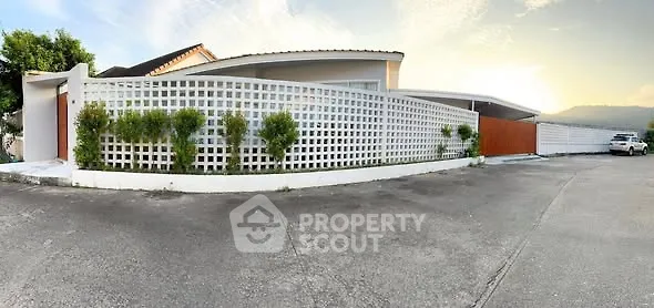 Modern house exterior with unique lattice fence and spacious driveway at sunset.