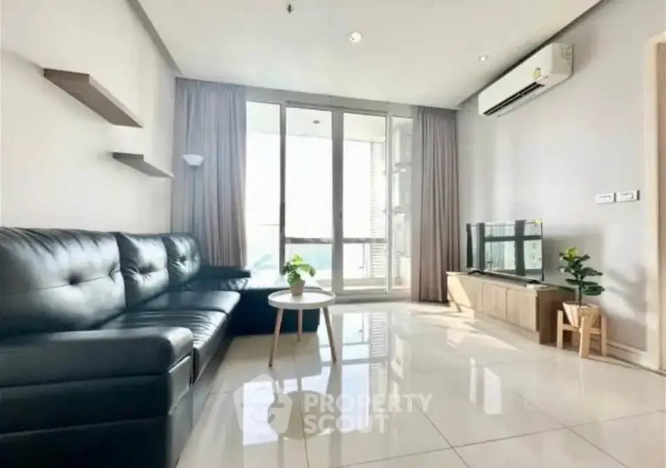 Modern living room with sleek black sofa, large windows, and air conditioning unit.