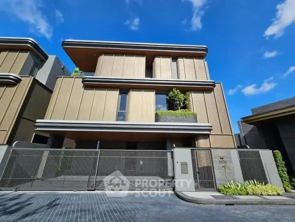 Luxurious modern three-story house with sleek design and gated entrance under clear blue sky.