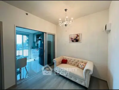 Chic living room with elegant chandelier and plush sofa, adjacent to a modern kitchen with balcony view.