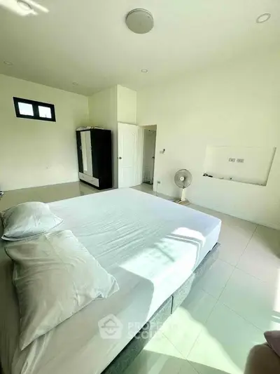 Spacious bedroom with natural light and minimalist decor, featuring a comfortable bed and wardrobe.