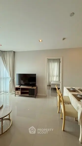Modern living room with dining area and TV, featuring elegant decor and natural light.