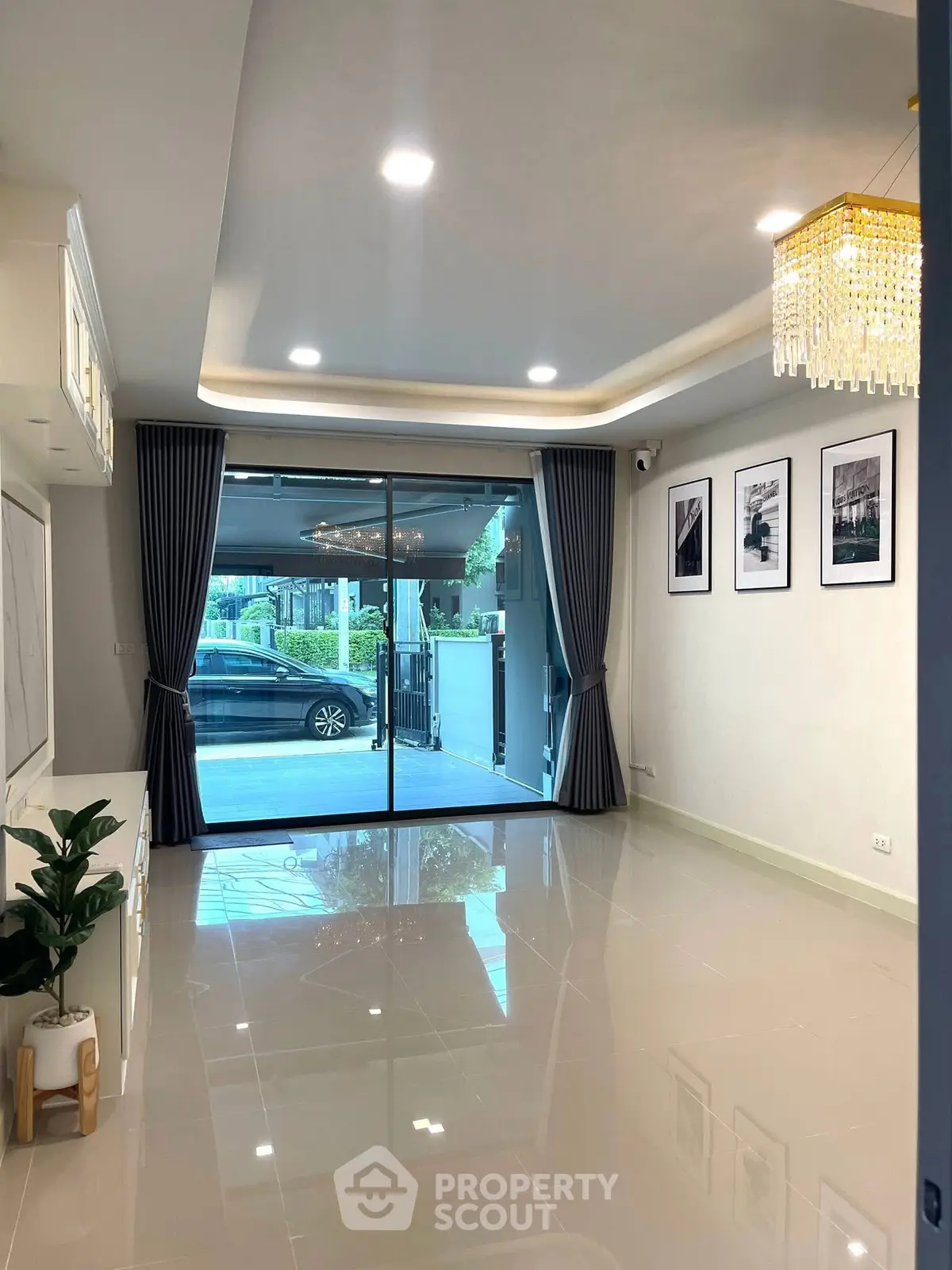 Spacious modern living room with elegant chandelier and large glass doors leading to a serene outdoor view.