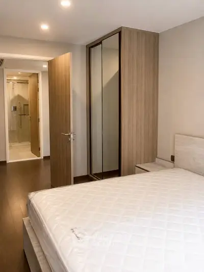 Modern bedroom with wooden flooring and ensuite bathroom in a stylish apartment.