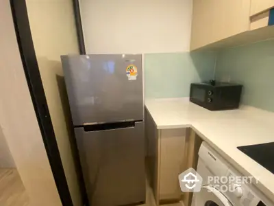 Modern kitchen with fridge, microwave, and washing machine in compact layout.