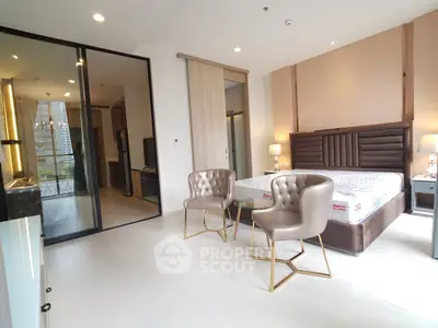 Luxurious modern bedroom with elegant chairs and glass partition, offering a glimpse into a stylish kitchen area.