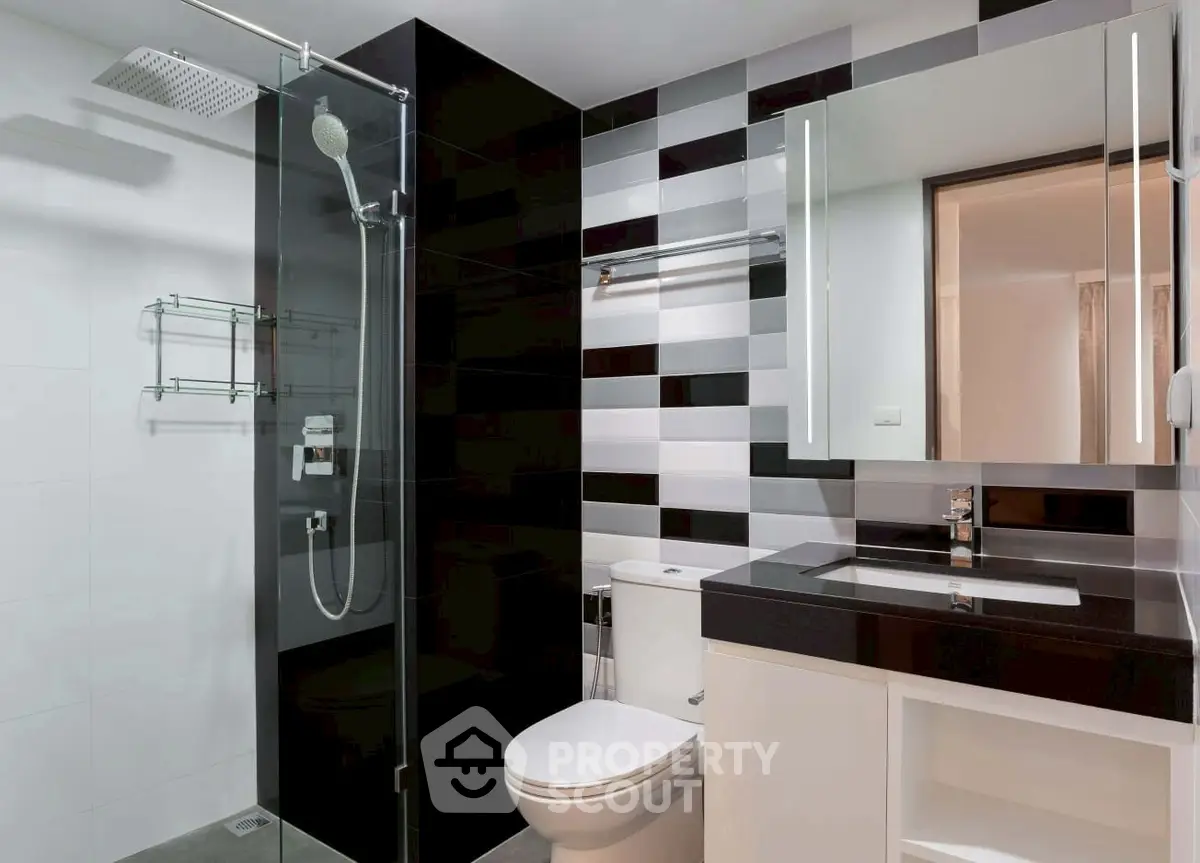 Modern bathroom with sleek black and white tiles and glass shower enclosure.