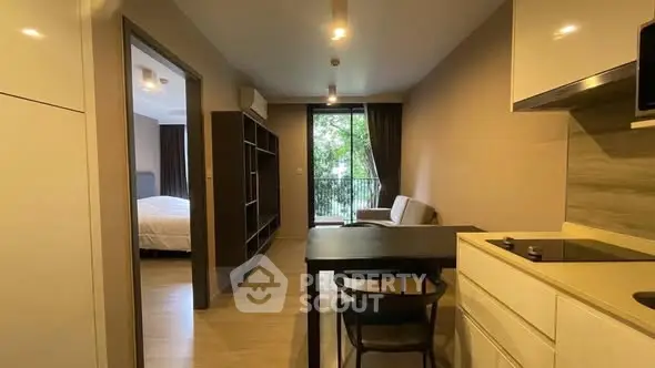 Modern apartment interior with open layout, featuring kitchen and living area leading to a balcony with greenery view.