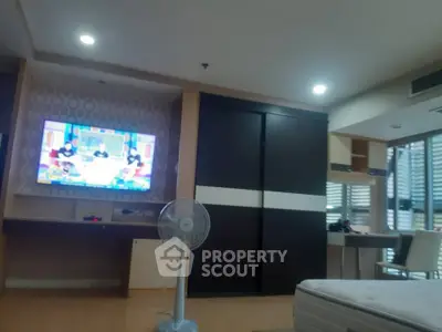 Spacious living room with modern decor and entertainment setup, featuring a wall-mounted TV and ample natural light.