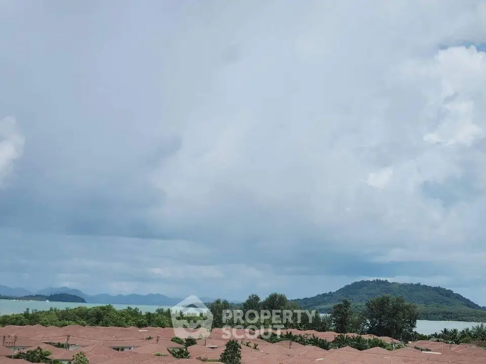 Scenic view of residential rooftops with lush greenery and distant mountains under a cloudy sky.