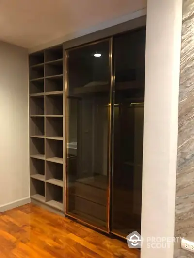 Modern walk-in closet with sleek glass doors and wooden flooring