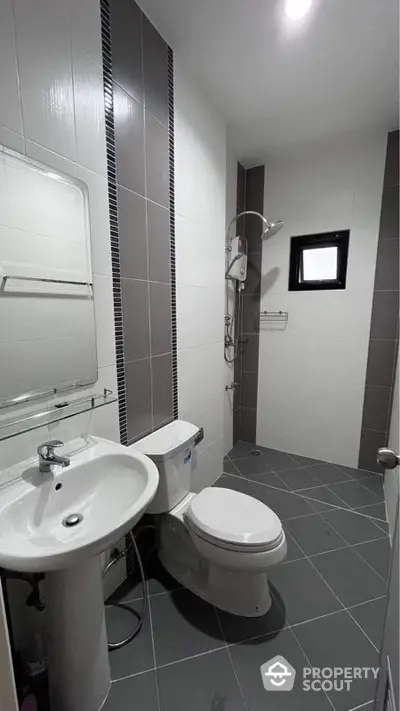 Sleek modern bathroom with a walk-in shower, pedestal sink, and wall-mounted mirror, featuring stylish gray tiling and a minimalist design.