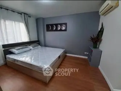 Modern bedroom with wooden flooring and moon phase artwork, featuring air conditioning and natural light.